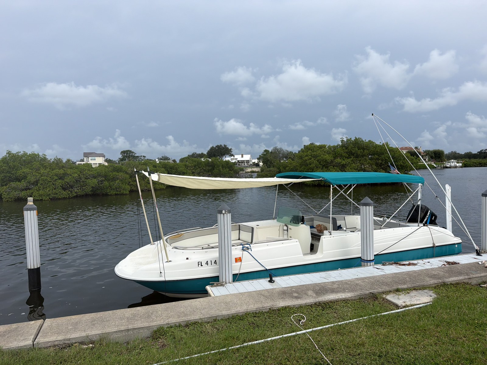Cream custom-fitted sunshade extending coverage beyond a teal Bimini top on a white motorboat.