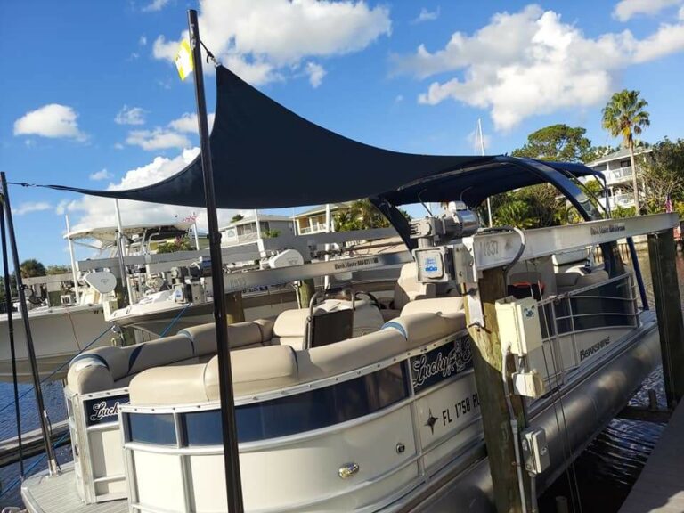 Black custom sunshade stretched above the seating area of a pontoon boat at the dock.