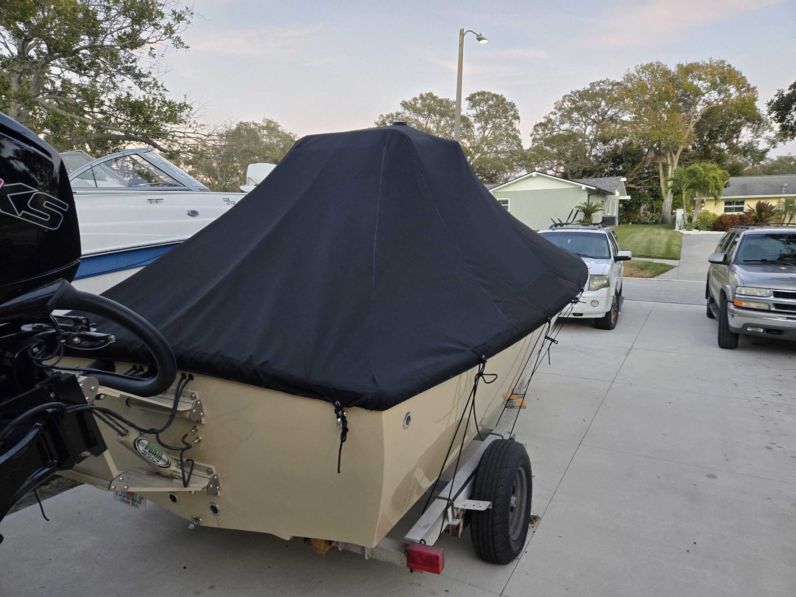Dark custom-fitted full boat cover secured around a center-console boat on a trailer.