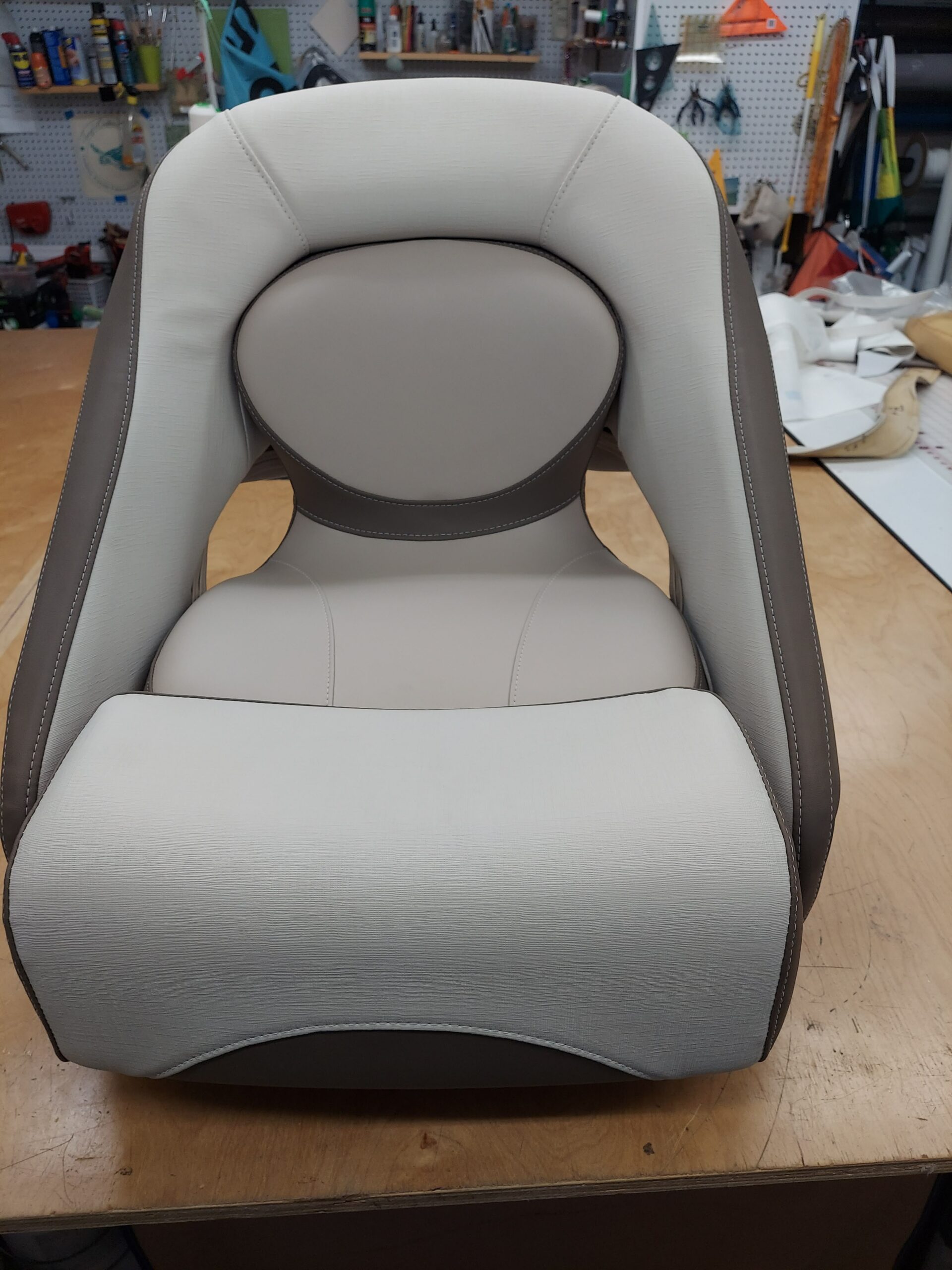 Finished marine helm seat upholstered in light gray and taupe vinyl with shaped panels and detailed stitching.